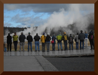 The backs of tourists waiting with cameras ready to photograph Old Faithful