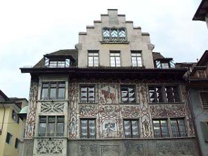 A five story building with many windows and elaborate carving on the walls along with painted decorations including a drawing of a man on a horse adorn the side of this building