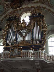 On a white balcony with painted railing sits a large wood and gilt frame for the organ in the imperial church of Maximilian