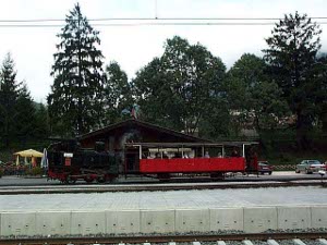 A lone red railroad car pulled by a black engine