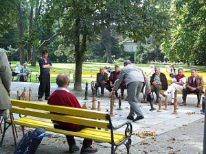 While onlookers watch from either side of the chessboard while sitting on park benches, the players walk around, moving the two-foot tall chess pieces on the outdoor chessboard