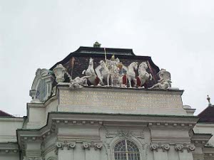 A heroic view of a conqueror in a chariot, the horses rearing over their foes; executed in marble atop the Hofburg