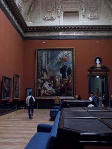 The museum gallery has very high walls painted a dark red, with a light rose patterned carpet, black tables and blue sofas for viewers.  The room is some 20 feet high, with a vaulted roof ornately decorated in white plaster