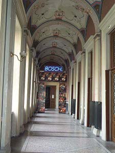Down a long arched gallery with marble floor at the end is a doorway with a blue neon sign reading 'BOSCH'