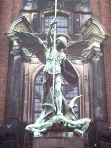 A heroic copper green statue of the winged angel Michael holding Satan down with his foot and driving a lance into Satan's back