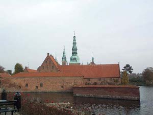 The red brick buildings in the foreground obscure the body of the castle, just the greenish towers are visible, and the wide moat provides big defenses