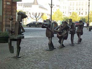 Down the center of a cobbled pedestrian walkway are five modern cubist-style bronze figures: a majorette and four musicians