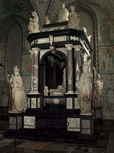 The tomb is surrounded by a marble canopy, with statues at the corners and on the roof over the tomb, all in black and brown