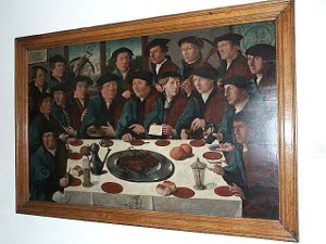 Some 18 men, dressed in green and brown robes with black berets, surround a formal banquet table.