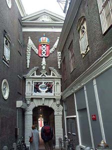 A heraldic device consisting of three vertical white X's on a field of red topped by a blue crown surmounts an elaborate door in an Amsterdam alley