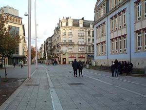 A nicely paved street with four-story buildings and pedestrians
