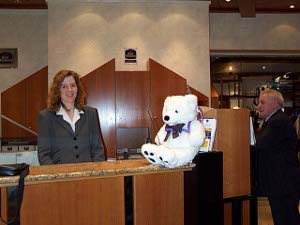Cuddles sits on the marble topped desk of the Best Western Hotel.  The clerk smiles for the camera while another guest looks on bemusedly