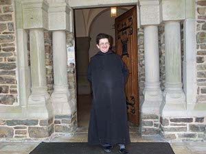 In front of the Abbey door stands a smiling Benedictine monk in a black habit