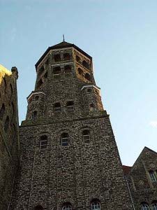 The tower apparently is at least 100 feet above the ground, with a mottled construction of alternating dark and light stones, and many arches and windows to an octagonal tower