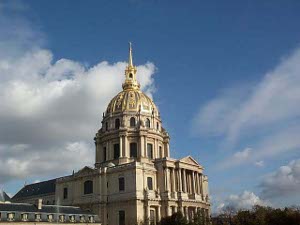 The massive gilt dome of the Hotel Les Invalides, a French national monument, rises high above the surrounding buildings, silhouetted against a bright blue sky dotted with white clouds