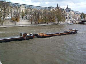 Two barges linked together moving up the Seine; the barges are low to fit under the bridges