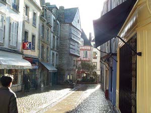 The sun sparkles after a recent rain shower, showing a four story overhanging stone building down the picturesque Quimper street