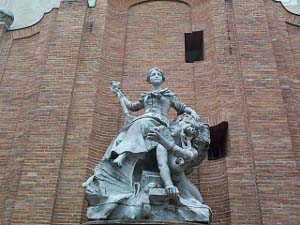 The statue shows a female figure sitting on the back of perhaps a river god; the color is greenish copper; the statue is in front of the huge red brick electric building