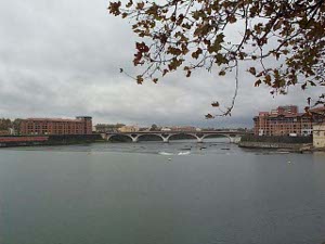 The Garonne River is wide, and in this view spanned by an arched bridge, with factory buildings on either bank