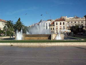 A fountain is in the middle of a large square, with a pool around, an exuberant central spray of water and frothy white geysers of water all around.