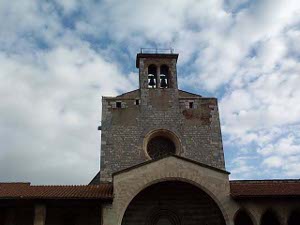 The two bells can be seen high in the tower above a round window; the sky has scattered clouds.
