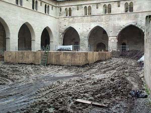 The dirt and mud is marked with the tracks of bulldozers, and a large concrete platform has been erected in the center of the courtyard.  The high gallery is visible above the huge arches at ground level