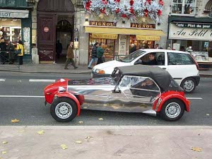 The car is a two seater roadster, with space for a big engine up front.  The hood and sides of the car are polished steel, while the fenders and front are bright red.  The car is a convertible, and the soft top is up, perhaps to protect from impending rain.
