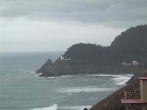 A forested hill, with two humps, descends abruptly to the ocean at Heceta Head, north of Heceta Beach.  Adjacent to the white lighthouse are two small red-roofed buildings