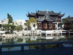 The photograph is from a walkway looking across a small pond at a pagoda-style building with curving black tile roof