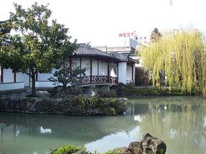 The Chinese Garden features a Chinese-style building, white with brown trim, over a large pond with rocks and a lovely willow tree