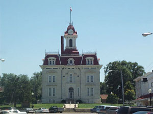 The bottom two stories of this three-story courthouse are made of cream-colored stone, the top floor with dormers and a red roof with a tall center tower