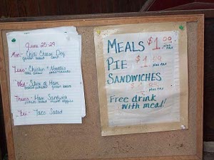 The menu is tacked to a small bulletin board resting on a chair.  The menu is for June 25-29.  Monday was Chili Cheese Dog, Garden Salad, corn.  Meals $1.00, Pie $1.00.  Free drink with meal.