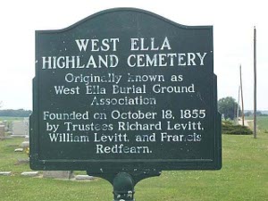 The paint is a little worn, but the white letters on the green metal cemetery sign read 'West Ella Highland Cemetery Originally known as West Ella Burial Ground Association Founded on October 18, 1855 by Trustees Richard Levitt, William Levitt, and Francis Redfearn.