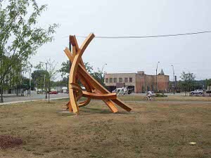 A large civic sculpture of orange steel beams, curved into a triangular edifice about twelve feet high, sits in an otherwise vacant lot in Benton harbor