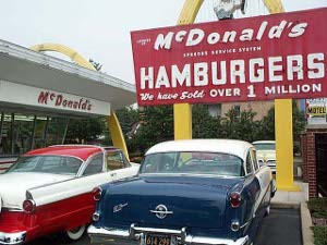 A 56 red and white Ford and a blue and white oldsmobile are classic cars parked in front of the original McDonald's museum in Des Plaines (15 cent hamburgers, over 1 million sold)