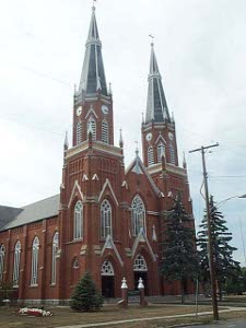 A large red brick building with white trim, the catholic church in Ottoville, Ohio has twin towers, each topped with an octagonal steeply pointed roof.
