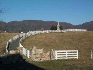 The very tall monument with a statue of an infantryman sits on top of a large hill, surrounded by a long approach road lined with a white fence