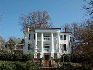A beautiful three story white home with tall columns extending from the ground up and balconies on both upper floors.