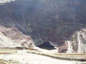 A deep pit, terraced in lower and lower, with a pool of water at the bottom, and rock sides colored brown and tan