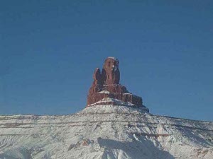 Above a snow white mesa and beneath an azure sky, a terra cotta colored monument reaches up starkly