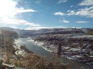 The sun glaring in the top left of the picture casts a brilliant glow on the river running through a snow-whitened Utah countryside