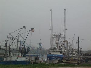 Against a gray and misty sky, two boats, perhaps shrimpers, are tied up at a dock in rural Louisiana