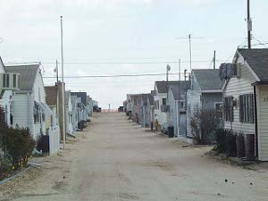 A sandy road down to the sea is flanked by dozens of nearly identical white cottages