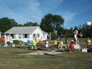In front of a small white house are some two dozen brightly painted cartoon figures, statues ranging from two to ten feet tall
