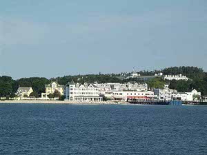 Between the light blue sky and the dark blue water, Mackinac Island shows attractive white buildings nestled against wooded green hillsides