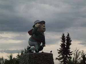 The caricature statue of Flin Flon, wearing a hat, with a backpack, down on one knee, right hand raised to look out, sits on top of a large stone pedestal