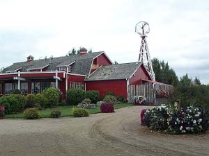 The large red-painted building has two floors, a windmill in back, and is surrounded by gardens