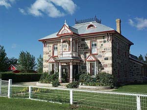 A beautiful two-story stone house, with brightly painted trim, and a neet grassy lawn.