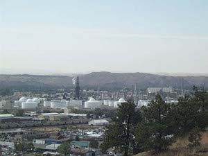 Taken from a hilltop, with evergreens in the right foreground, the picture shows Billings stretched out in the valley below, with the white painted refinery tanks in the middle ground