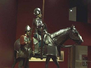 A full scale model of a conquistador carrying a lance astride a horse, both wearing 18th century armor